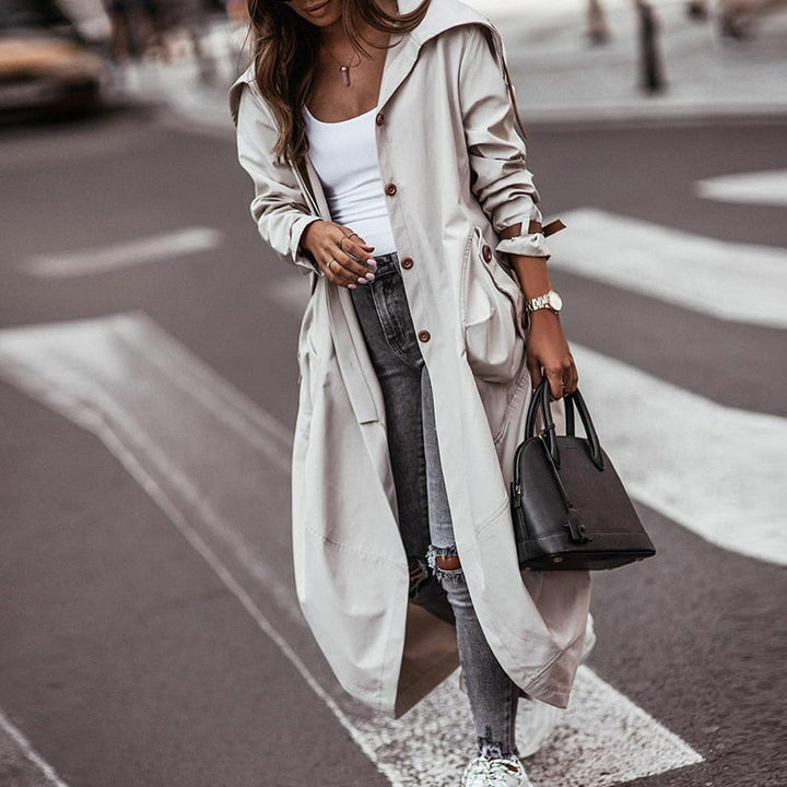 Elegante grijze lange trenchcoat voor dames met functionele zakken, perfect voor stijlvolle voorjaars- en najaarsmode.